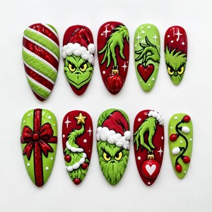 Könnte beinhalten: Ein Set aus zehn mandelförmigen Press-on-Nägeln mit weihnachtlichen Motiven. Die Designs zeigen eine grüne Figur mit Weihnachtsmütze, rot-grüne Zuckerstangenstreifen, ein Geschenk mit roter Schleife, Lichterketten und Weihnachtskugeln.