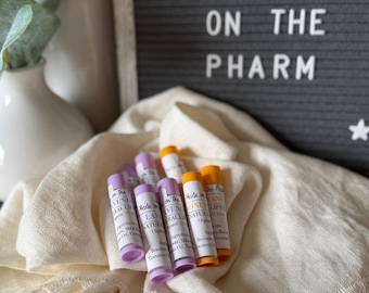May include: Four small tubes of lip balm with labels that say "Made on the Pharm" and list ingredients. The labels are in purple, yellow, and orange. The tubes are on a white, fluffy, fringed blanket.