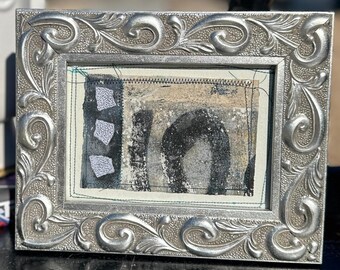 Mixed media artwork in a silver ceramic frame with an easel back