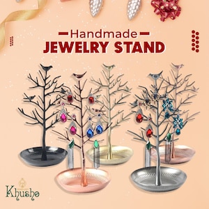 May include: Handmade jewellery stand with a tree branch design and a small bird on each branch. The stand is available in four colours: black, copper, gold, and silver. The stand is decorated with colourful earrings.
