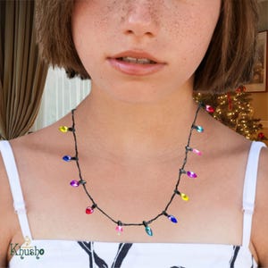 Könnte beinhalten: Eine Halskette mit bunten Weihnachtsbeleuchtungen auf einem schwarzen Kabel. Die Lichter sind in verschiedenen Farben, darunter Rot, Blau, Gelb und Grün. Die Halskette wird um den Hals getragen.