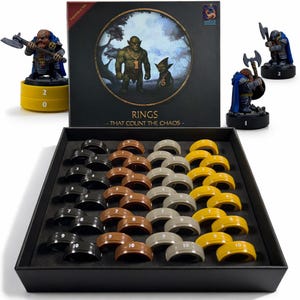 May include: A board game set with a black box featuring the text "RINGS - THAT COUNT THE CHAOS." The set includes miniature figurines and a tray of numbered rings in black, brown, gray, and yellow. The figurines are of fantasy characters.