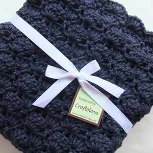 May include: A navy blue crocheted baby blanket with a white satin ribbon tied in a bow and a brown tag that reads "Handmade with love, Craftolove, www.craftolove.etsy.com"