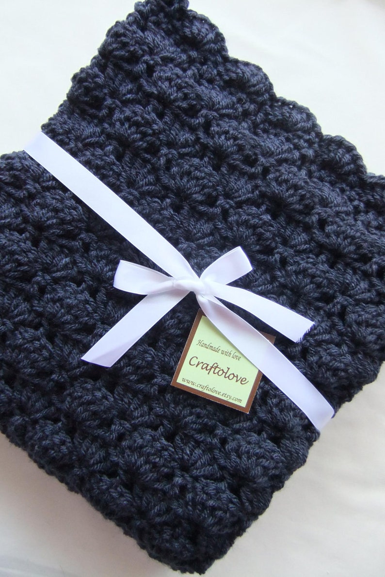 May include: A navy blue crocheted baby blanket with a white satin ribbon tied in a bow and a brown tag that reads "Handmade with love, Craftolove, www.craftolove.etsy.com"