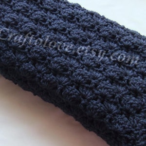 May include: A navy blue crocheted blanket with a textured, floral pattern. The blanket is folded in half and is lying on a white surface.
