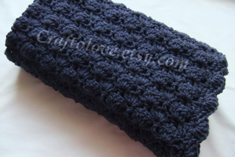 May include: A navy blue crocheted blanket with a textured, floral pattern. The blanket is folded in half and is lying on a white surface.