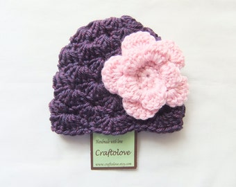 May include: Purple crocheted baby hat with a pink crocheted flower on top. The hat has a tag that says "Handmade with love Craftlove www.craftlove.etsy.com".