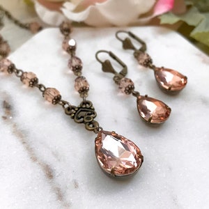 May include: A delicate blush pink crystal necklace and matching earrings set with a teardrop pendant and bronze chain.