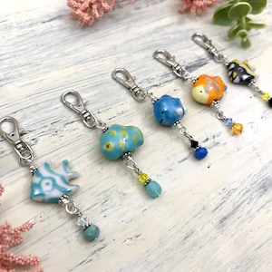 May include: Five colorful fish charm keychains with silver chains and crystal beads. The fish are blue, orange, yellow, and white with blue and yellow accents.