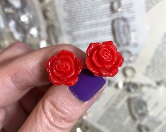 May include: A pair of red rose stud earrings. The earrings are made of plastic and have a shiny finish.
