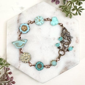 May include: A turquoise blue bracelet with a bird charm, flower charms, and a lobster clasp closure.