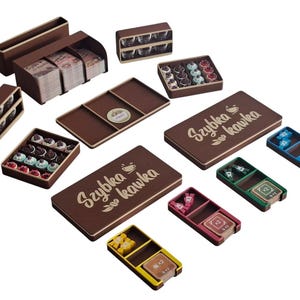 Könnte beinhalten: Eine Sammlung brauner Holzspielkomponenten, darunter Schachteln, Tabletts und Behälter. Einige Schachteln enthalten kleine, farbenfrohe Spielsteine. Der Text "Szybka Kawka" ist auf eine braune Schachtel gedruckt.