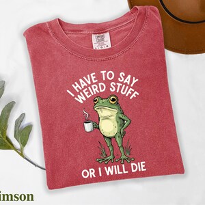 A red t-shirt with a cartoon frog holding a cup of coffee and the text "I HAVE TO SAY WEIRD STUFF OR I WILL DIE" printed on it.