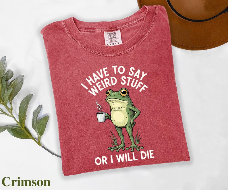 A red t-shirt with a cartoon frog holding a cup of coffee and the text "I HAVE TO SAY WEIRD STUFF OR I WILL DIE" printed on it.