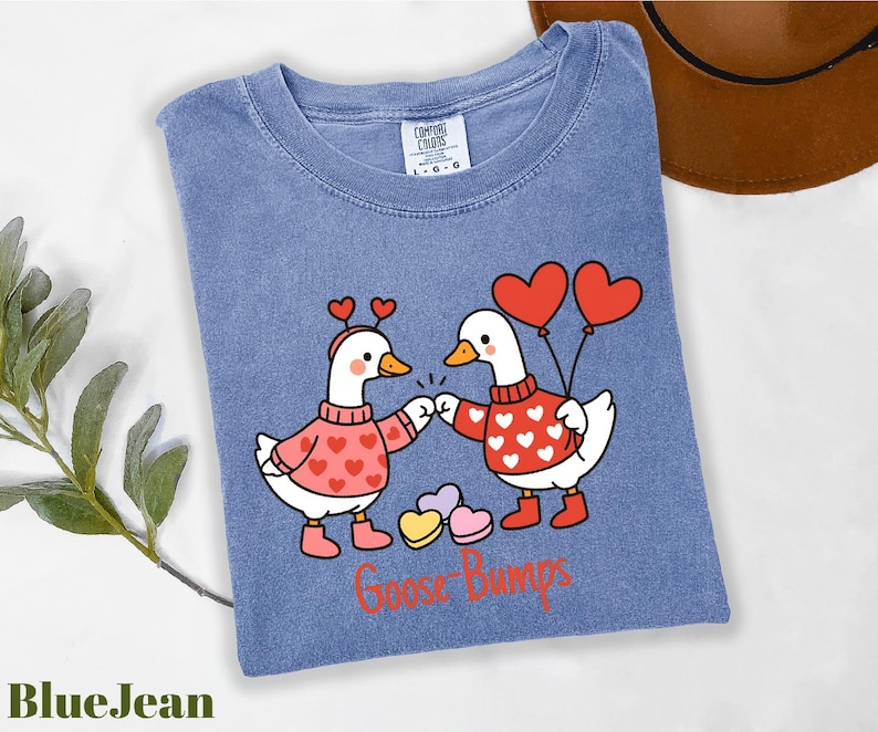 A blue t-shirt with a graphic design of two cartoon geese holding heart-shaped balloons and the text "Goosebumps" below them.