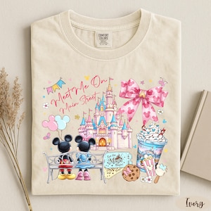A t-shirt with a Disney-themed design, including Mickey Mouse, Minnie Mouse, a castle, and various Disney-related items such as a cup of ice cream and a cookie.
