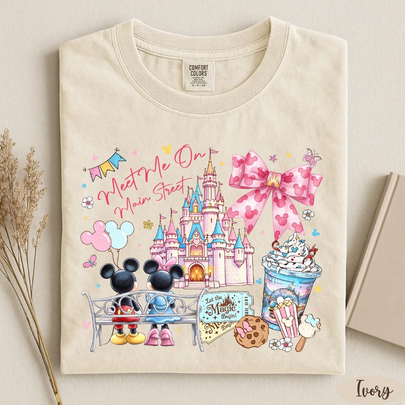 A t-shirt with a Disney-themed design, including Mickey Mouse, Minnie Mouse, a castle, and various Disney-related items such as a cup of ice cream and a cookie.