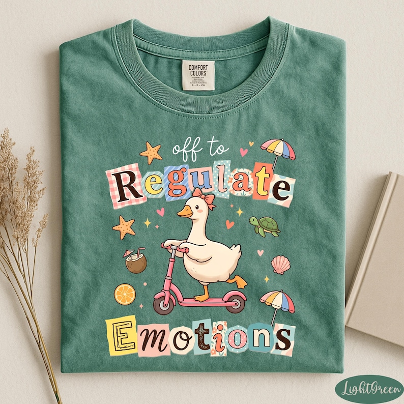 A green t-shirt with a colorful graphic design featuring a duck riding a scooter, surrounded by various objects such as umbrellas, flowers, and a book.