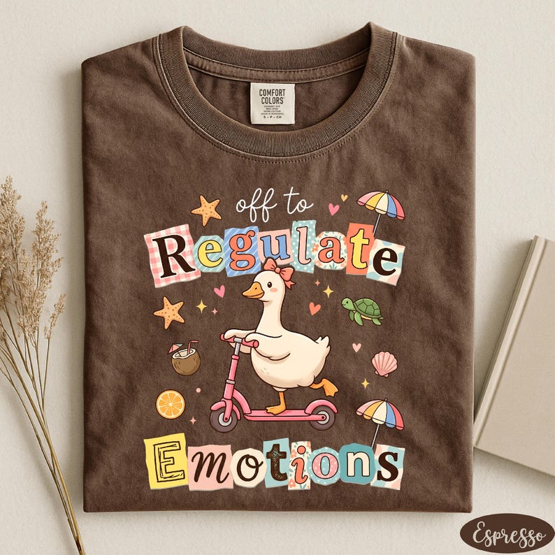 a brown t-shirt with a colorful graphic design depicting a duck riding a pink scooter, surrounded by various objects such as a star, umbrella, and seashell.