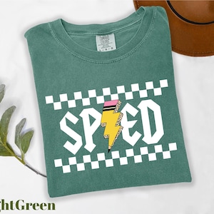 a green t-shirt with a checkered pattern and the word "SPEED" printed on it, along with a lightning bolt graphic. The t-shirt is placed on a white surface, and there is a brown hat visible in the background.