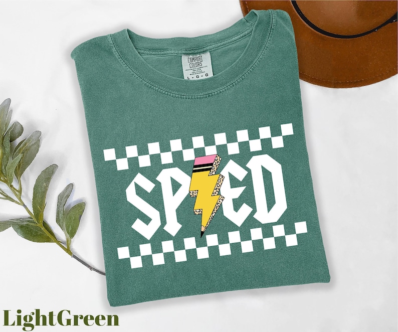 a green t-shirt with a checkered pattern and the word "SPEED" printed on it, along with a lightning bolt graphic. The t-shirt is placed on a white surface, and there is a brown hat visible in the background.