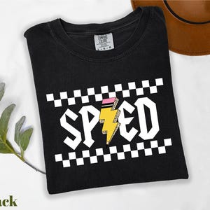 A black t-shirt with a checkered pattern and the word "SPEED" printed on it, along with a brown hat and a green plant.