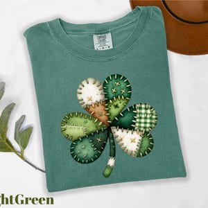 May include: Light green t-shirt with a large, stitched shamrock design. The shamrock features patches of white, tan, and various shades of green, including a checkered pattern. The text "LightGreen" is at the bottom.