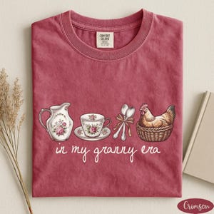A red t-shirt with a printed design of a tea set and a chicken, accompanied by the text "in my granny era"