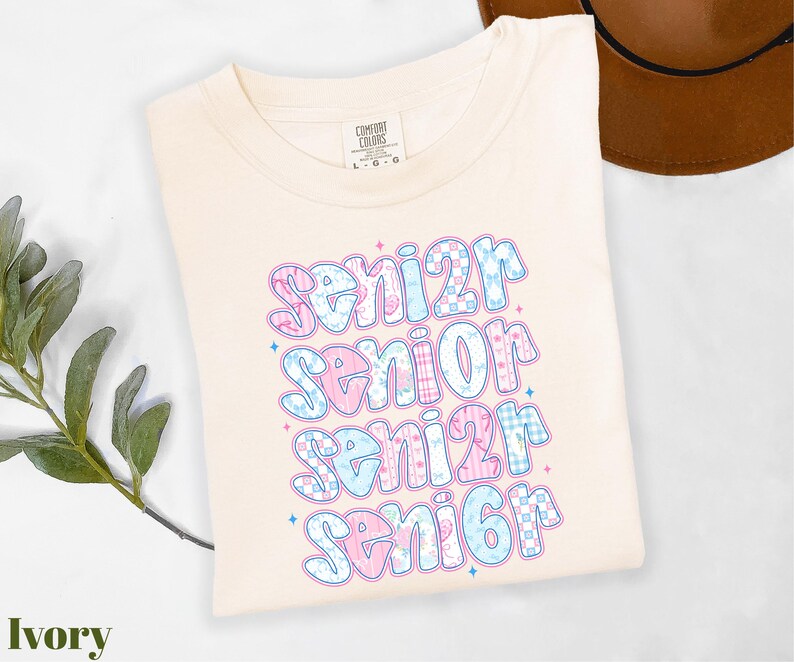 A white t-shirt with a colorful text design that says "senior senior senior" printed on it, along with some decorative elements.