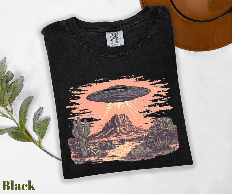 a black shirt with a picture of an alien flying over a desert
