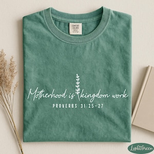 A green t-shirt with white text and a small plant graphic, along with a book and some dried flowers, arranged on a white surface.