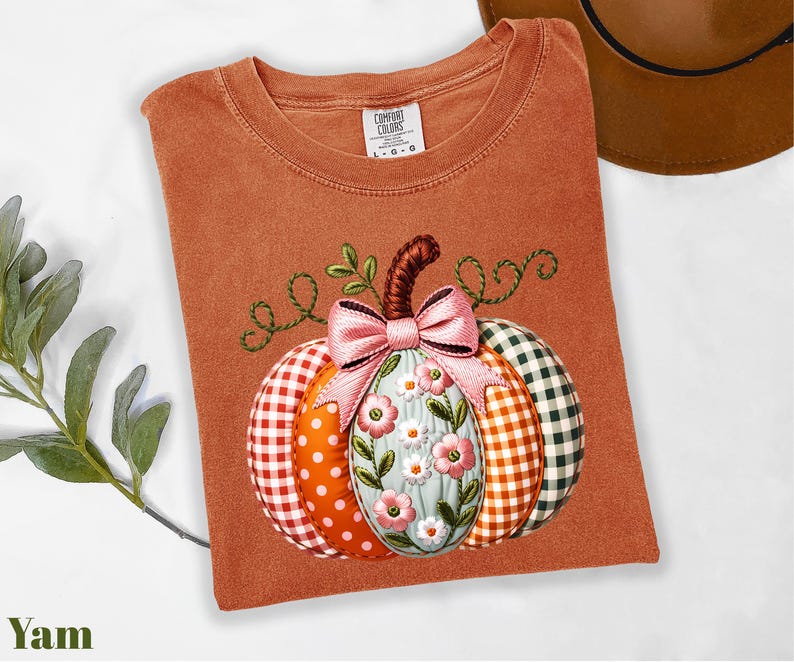 a brown t-shirt with a colorful pumpkin embroidered on it, along with a hat and some greenery.
