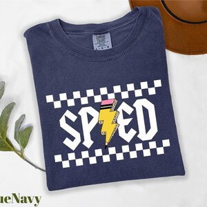 A navy blue t-shirt with a graphic design featuring a lightning bolt and the word "SPEED" printed on it, along with a brown hat and a green plant in the background.