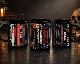 May include: Three black ceramic mugs with a wraparound design featuring VHS tape spines of classic horror movies. Titles include "Friday the 13th," "Halloween," and "Hellraiser." Each mug has a black handle and a dark background.