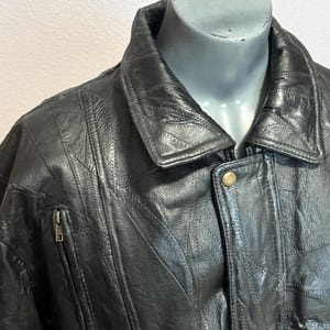 May include: Black leather jacket with a notched collar and a zipper pocket on the chest. The jacket has a button closure and a quilted design. The jacket is displayed on a mannequin.