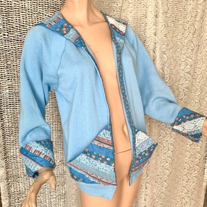 May include: A light blue hooded sweatshirt with a patchwork design on the front and sleeves. The patchwork is made of various blue and pink floral fabrics.