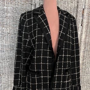 K&ouml;nnte beinhalten: Schwarzer und wei&szlig;er Tweed-Blazer mit Fransenbesatz. Der Blazer hat einen Kragen und lange &Auml;rmel.
