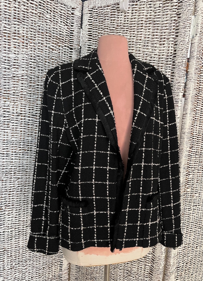 K&ouml;nnte beinhalten: Schwarzer und wei&szlig;er Tweed-Blazer mit Fransenbesatz. Der Blazer hat einen Kragen und lange &Auml;rmel.