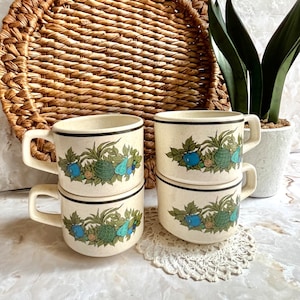 May include: Four white ceramic mugs with a green, blue, and brown floral design. The mugs are stacked in pairs and have a black rim.