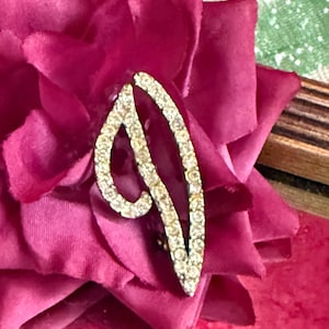 Peut inclure: Gros plan sur une fleur en tissu magenta foncé avec une broche incurvée et étincelante de couleur argentée. La broche est incrustée de petits cristaux transparents. Les pétales de la fleur sont superposés et texturés.