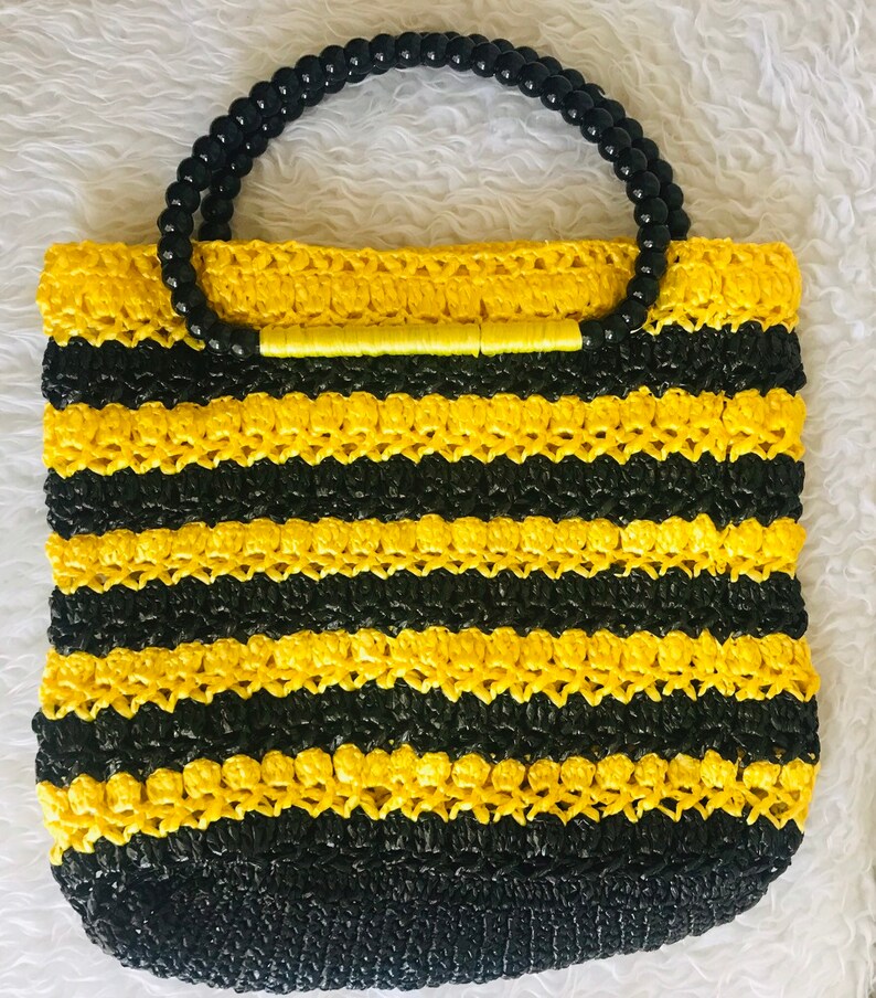 May include: A yellow and black striped crocheted tote bag with a black beaded handle.