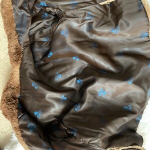 Pu&ograve; includere: Un cappotto in finta pelliccia marrone con fodera in raso. La fodera interna &egrave; di colore marrone scuro con un motivo di piccoli disegni floreali blu. L'esterno del cappotto ha un aspetto ispido e strutturato.