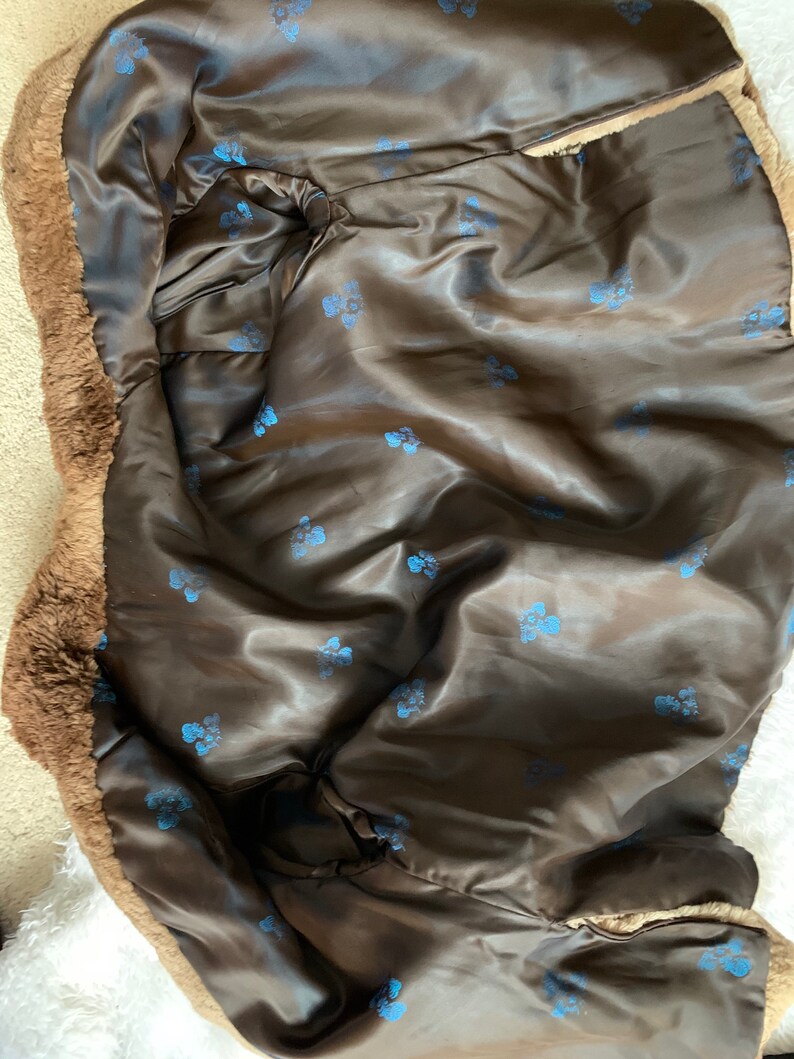 Pu&ograve; includere: Un cappotto in finta pelliccia marrone con fodera in raso. La fodera interna &egrave; di colore marrone scuro con un motivo di piccoli disegni floreali blu. L'esterno del cappotto ha un aspetto ispido e strutturato.