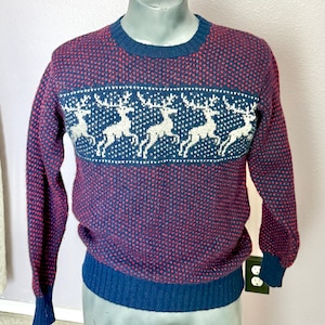 May include: A burgundy and navy blue sweater with a reindeer pattern. The sweater features a crew neck, long sleeves, and a ribbed hem and cuffs. The reindeer design is white on a navy blue band across the chest.