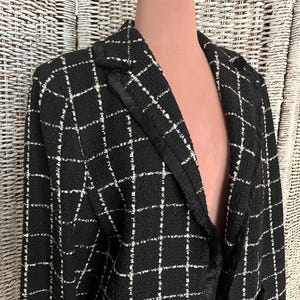 K&ouml;nnte beinhalten: Schwarz-wei&szlig; kariertes Blazer mit Fransenbesatz. Der Blazer hat einen klassischen Schnitt und einen doppelreihigen Verschluss.