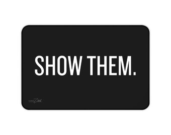 Könnte beinhalten: Schwarzes rechteckiges Mousepad mit abgerundeten Ecken. Die Worte "SHOW THEM." sind in großer, weißer, serifenloser Schrift mittig aufgedruckt. Eine Signatur befindet sich in der unteren linken Ecke.