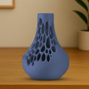 May include: A blue decorative vase with a unique open-work design. The vase has a bulbous base and a cylindrical neck. The open design creates a honeycomb-like pattern. The vase is made of a solid material and sits on a wooden surface.