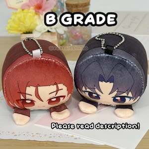 May include: Two plush character charms with metal ball chains. One features red hair and brown eyes, the other has dark hair and blue eyes. Both have small arms and are labeled B GRADE with the text Please read description! visible in the image.