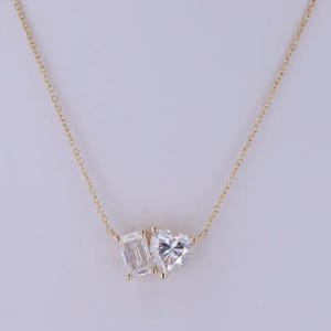 May include: A gold necklace with two clear gemstones: an emerald-cut and a heart-shaped stone. The gemstones are set close together, creating a unique pendant design. The necklace has a fine chain, perfect for everyday wear.