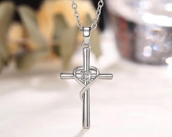 Könnte beinhalten: Halskette mit einem silberfarbenen Kreuzanhänger. Das Kreuz hat ein herzförmiges Design mit einem kleinen, klaren Edelstein in der Mitte. Die Halskette ist ebenfalls silberfarben.
